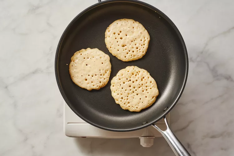 The pancake on the pan with bubbles forming on top